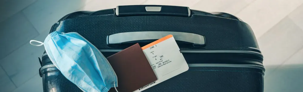 Face mask, passport, and boarding pass on top of wheeled luggage
